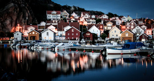 Boats moored on sea against houses at dusk