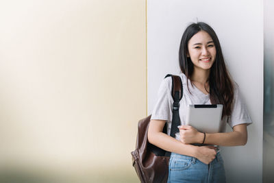 Portrait of a smiling young woman standing against wall