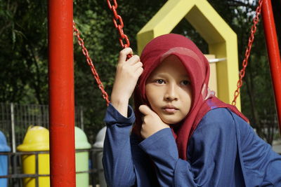 Girl looking away while holding chain in playground