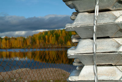 Close-up of metal railing by lake against sky