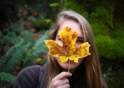 Portrait of woman holding yellow leaf against face 
