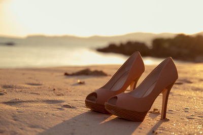 Close-up of shoes on sand at beach against sky