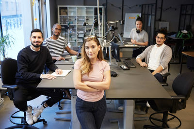 Portrait of confident female and male entrepreneurs at desk in creative office