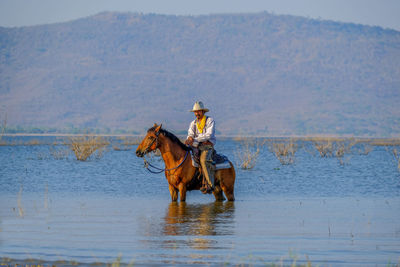 Mature man riding horse in lake against mountain