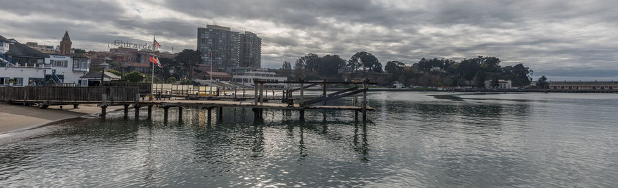 View of city at waterfront against cloudy sky