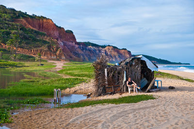 Man sitting on chair by tent at beach against sky