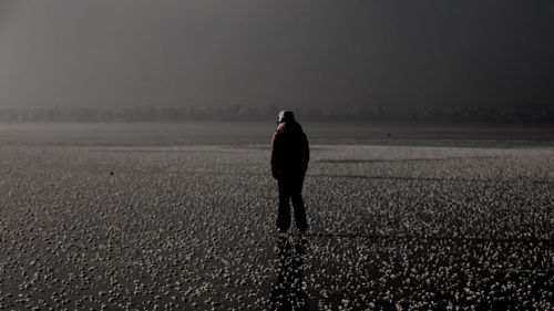 Rear view of woman standing on field against sky during winter