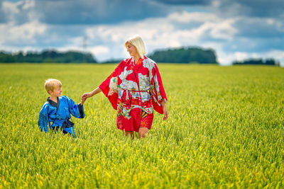 Smiling mother and son holding hands while standing by plants on field