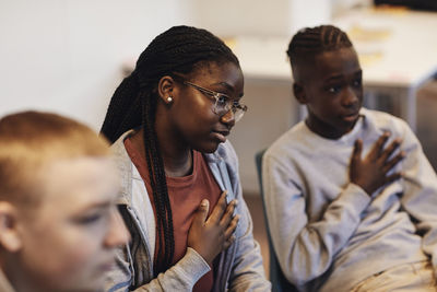 Teenage boy and girl sitting with hands on chests by male friend during group therapy in school