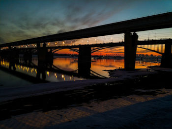 Silhouette bridge over river against sky at sunset