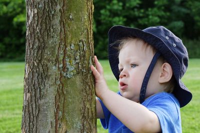 Cute baby boy wearing hat standing by tree at park