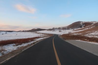 Empty road amidst snowcapped mountains against sky