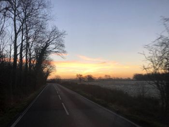 Road by trees against sky during sunset