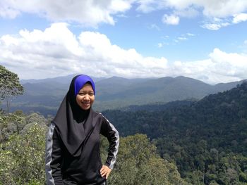 Portrait of smiling young woman standing on mountain against sky