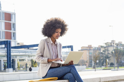 Businesswoman working on laptop while sitting on retaining wall