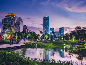 Lake and modern buildings against sky in city at dusk