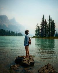 Rear view of woman standing on rock by lake against sky