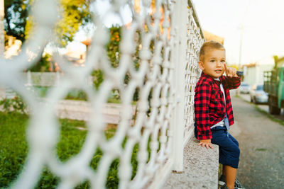 Boy looking away while standing against fence