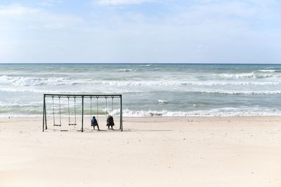 People on a swing at the beach against sky staring out at the mediterranean sea.