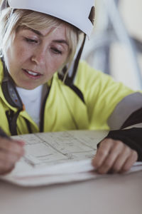 Female building contractor writing while analyzing floor plan at construction site