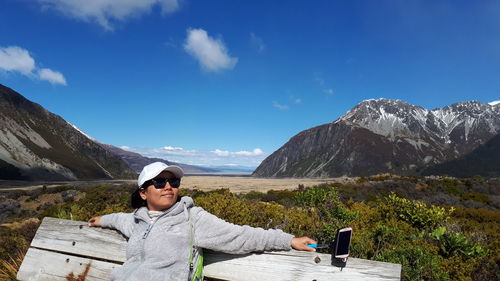 Young woman sitting on mountain against sky