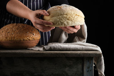 Female hands holding round baked wheat flour bread over wooden table, close up
