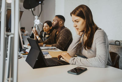 Male and female hackers working on laptop at table in startup company