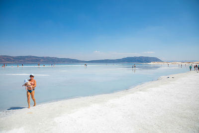 Rear view of woman standing on beach against blue sky