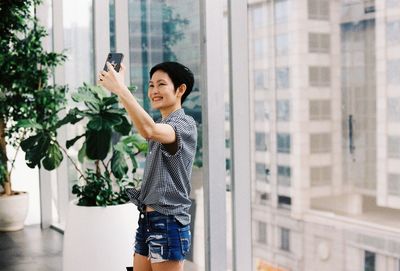 Woman taking selfie through mobile phone against window