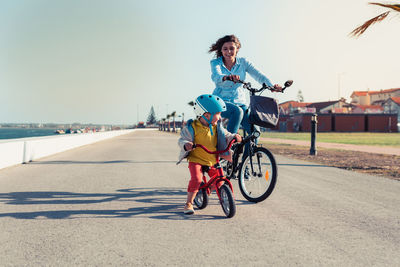 Woman and son riding bicycle on road in city