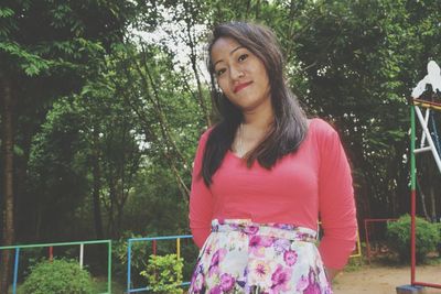 Portrait of woman standing against trees at park