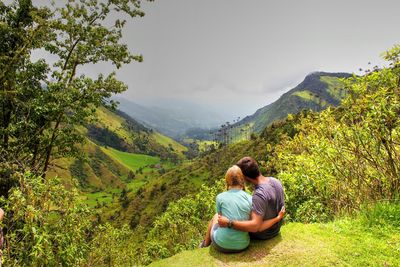 High angle rear view of couple embracing while sitting on mountain