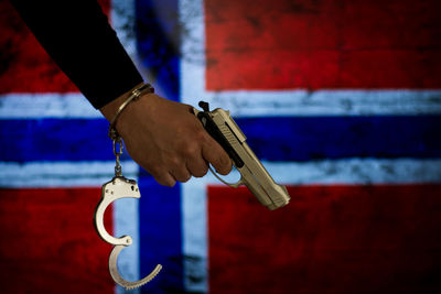 Cropped hand with handcuffs holding gun against norwegian flag