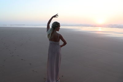 Woman standing at beach against sky during sunset