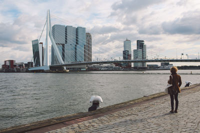 Rear view of woman standing at harbor against erasmusbrug in city