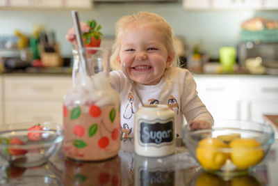 Portrait of cute girl holding strawberry in kitchen at home