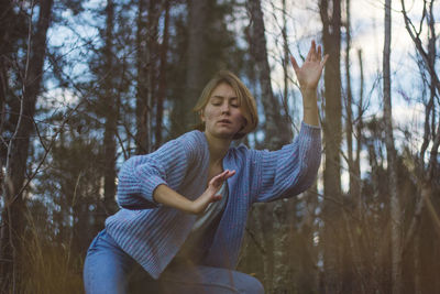 Young woman with short hair dancing against trees in forest