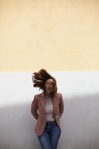 Portrait of a smiling young woman standing against wall