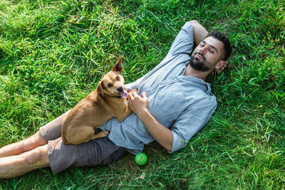 Attractive european man is resting on grass with his cute little dog on a summer sunny day.