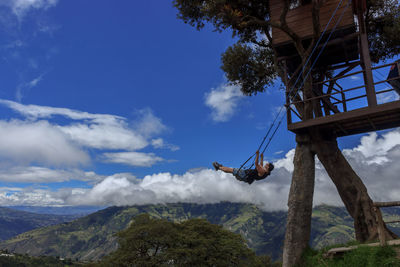 Low angle view of woman playing on swing against sky