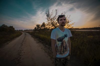 Young man standing on road against sky during sunset