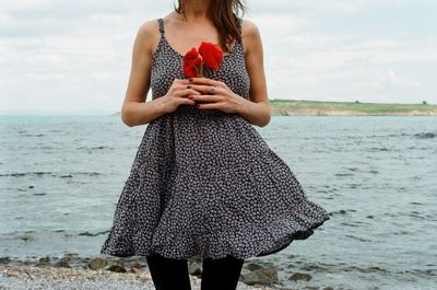 Midsection of woman holding red poppies while standing at beach