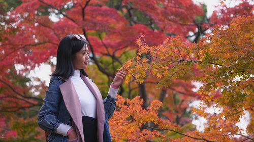 Young woman looking at orange leaves on tree during autumn