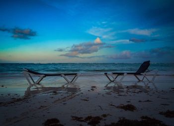 Deck chairs on beach against sky at dusk