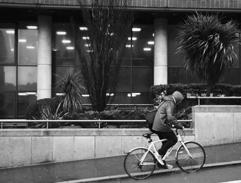 Side view of man riding bicycle on wet road against building