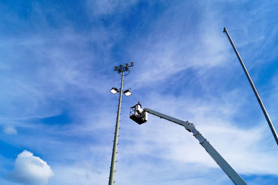 Low angle view of cherry picker by floodlight against sky