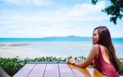 Portrait of young woman looking at sea against sky