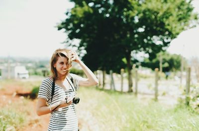 Young woman holding camera while sitting on tree