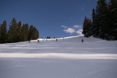 People skiing on snow covered field against sky