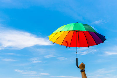 Low angle view of hand holding multi colored umbrella against sky